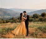 Couple in elegant gown embracing on open scenic hillside meadow